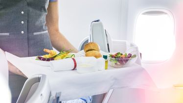 Ein Flugbegleiter serviert ein Essenstablett mit Salat, Brötchen und Garnelen von einem Foodservice in einem Flugzeug