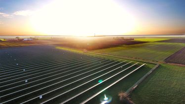 Solarpark mit langen Reihen von Solarmodulen bei Sonnenaufgang, strahlender Himmel im Hintergrund