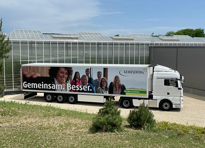 Ein Gemüsering-Lkw mit dem Slogan "Gemeinsam. Besser." steht vor einem modernen Gewächshaus und zeigt die Vermarktung im Obst und Gemüsehandel