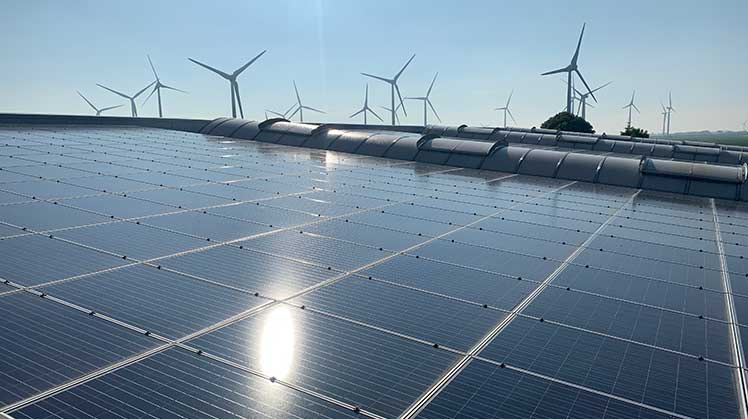 Weitläufige Solaranlagen auf einem Dach mit Windrädern im Hintergrund, betrieben von Green Energy